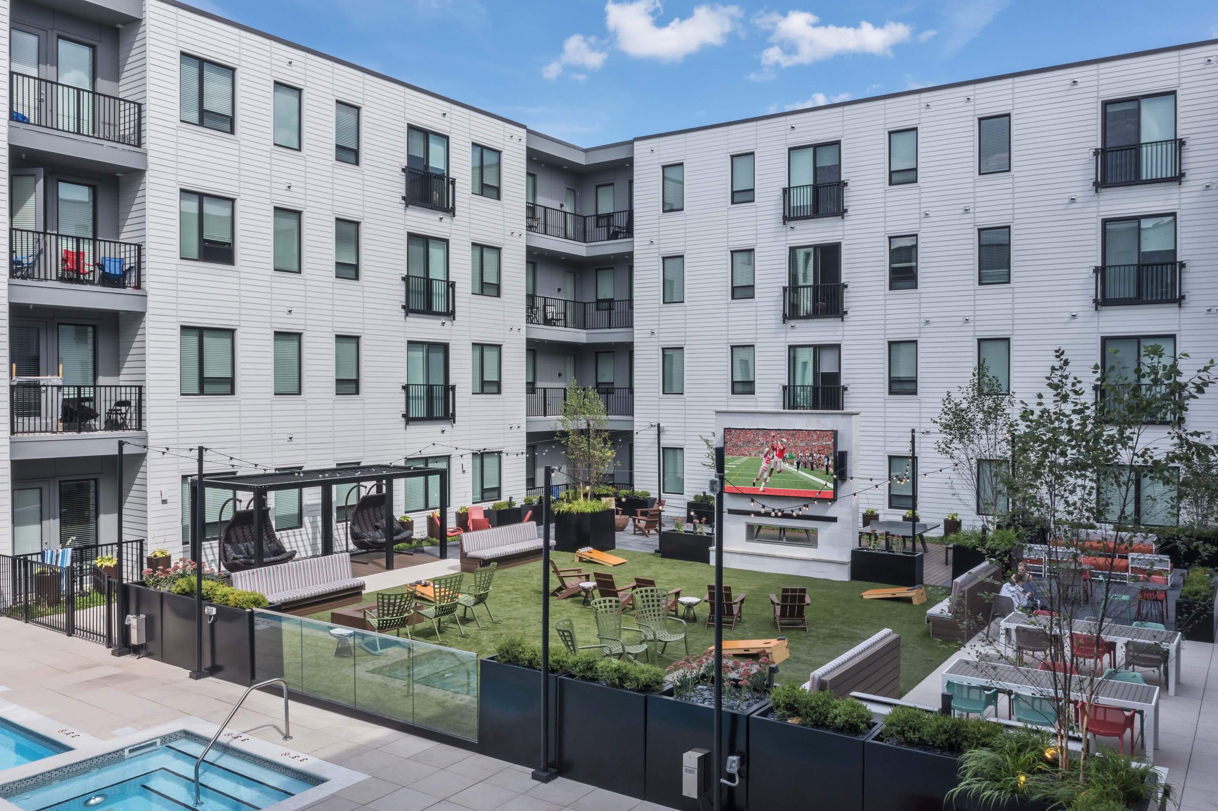 Lumen on Ninth Student Living Apartments Modern apartment courtyard with outdoor seating, a large TV showing sports, and a pool in the foreground.