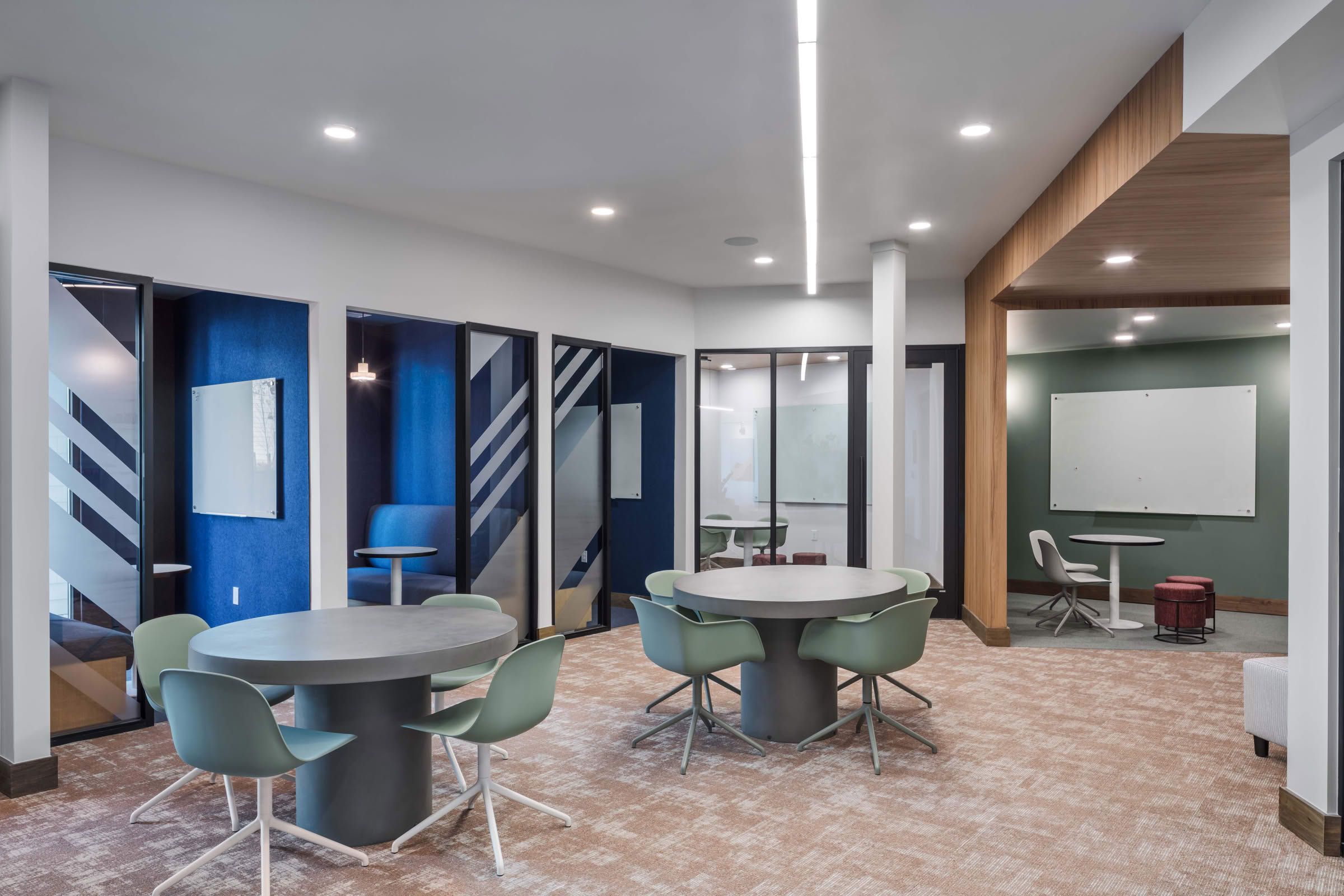 Lumen on Ninth Student Living Apartments Modern office space with round tables, green chairs, private booths, and whiteboards on the walls.