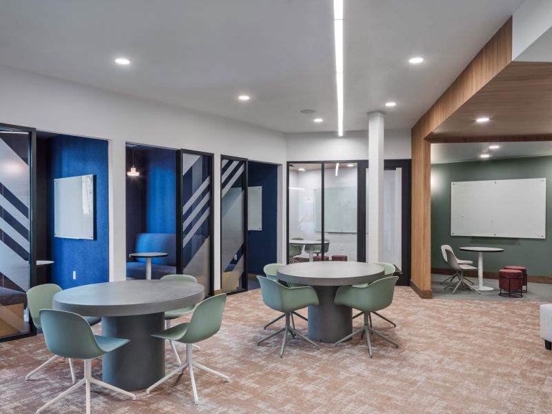 Lumen on Ninth Student Living Apartments Modern office space with round tables, green chairs, private booths, and whiteboards on the walls.