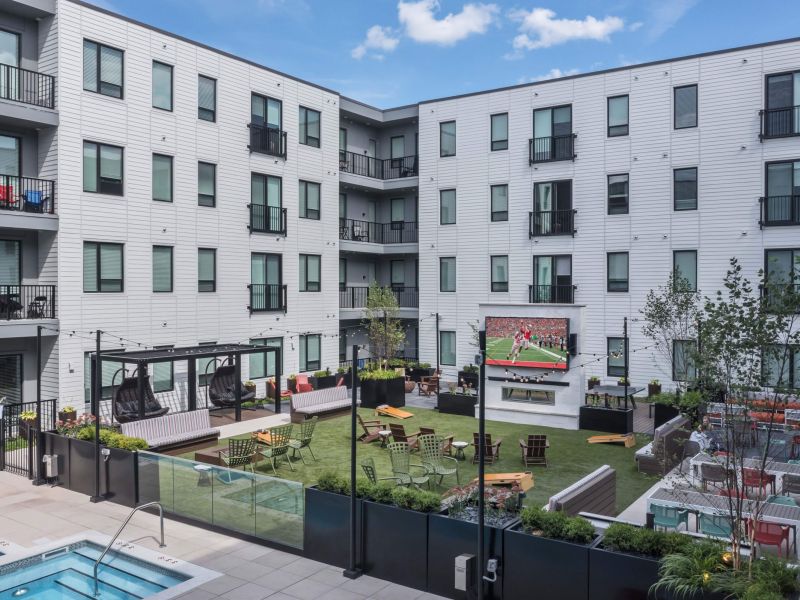 Lumen on Ninth Student Living Apartments Modern apartment courtyard with outdoor seating, a large TV showing sports, and a pool in the foreground.